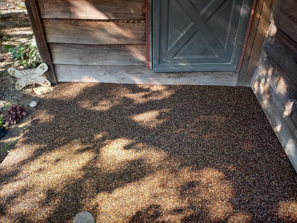 A gravel walkway leads to a rustic wooden cabin with a grey door and a butterfly-shaped garden decoration.