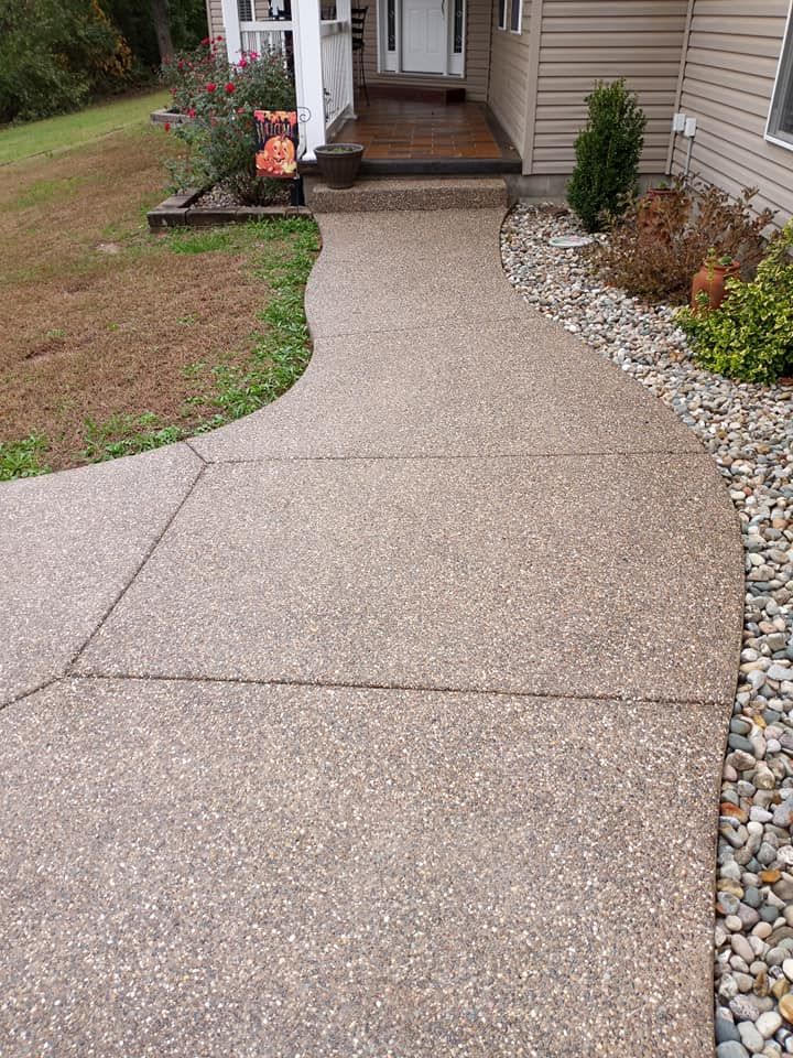 A concrete sidewalk with an exposed aggregate finish leading to a residential house entrance.