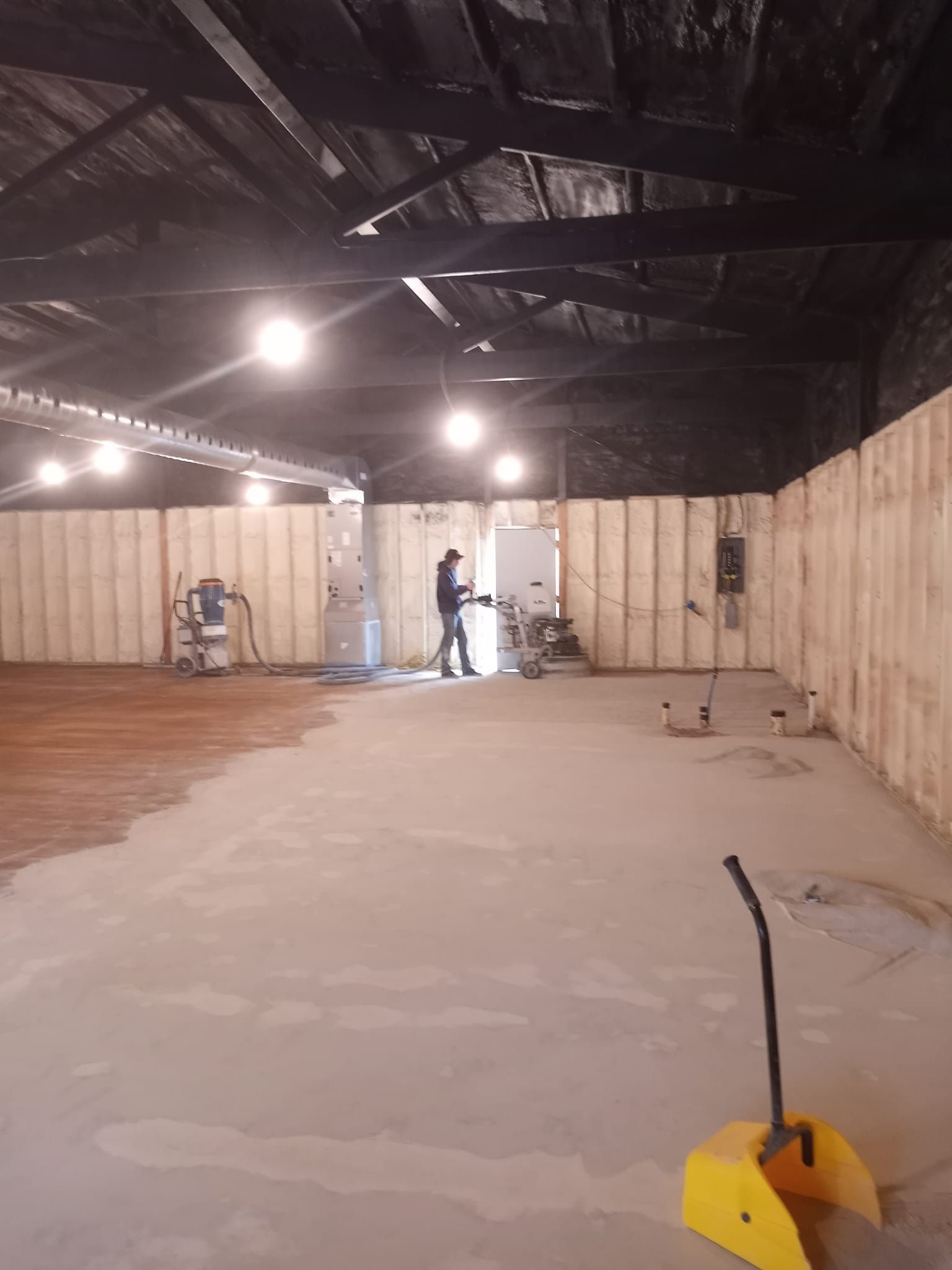 A worker uses industrial equipment to refinish a large, open space with insulation panels on the walls and dark ceilings.