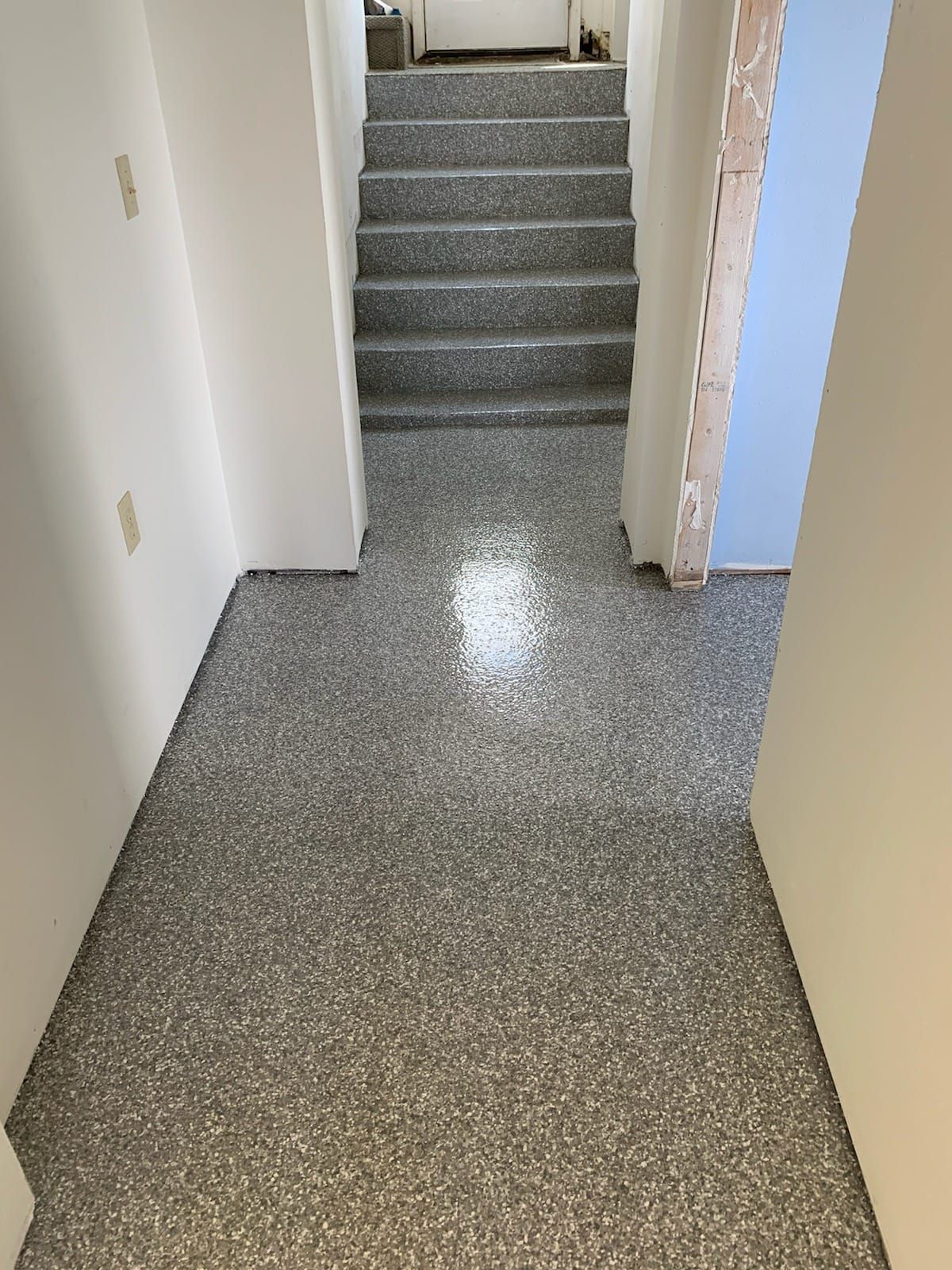 A hallway with gray speckled epoxy flooring leads to a set of matching stairs.
