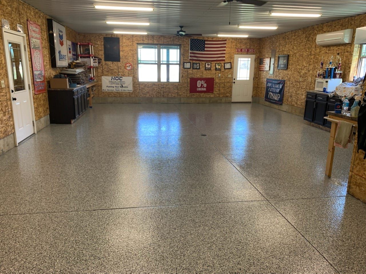 A spacious garage with a grey speckled epoxy floor, wood-paneled walls, multiple doors, windows, and ceiling lights.