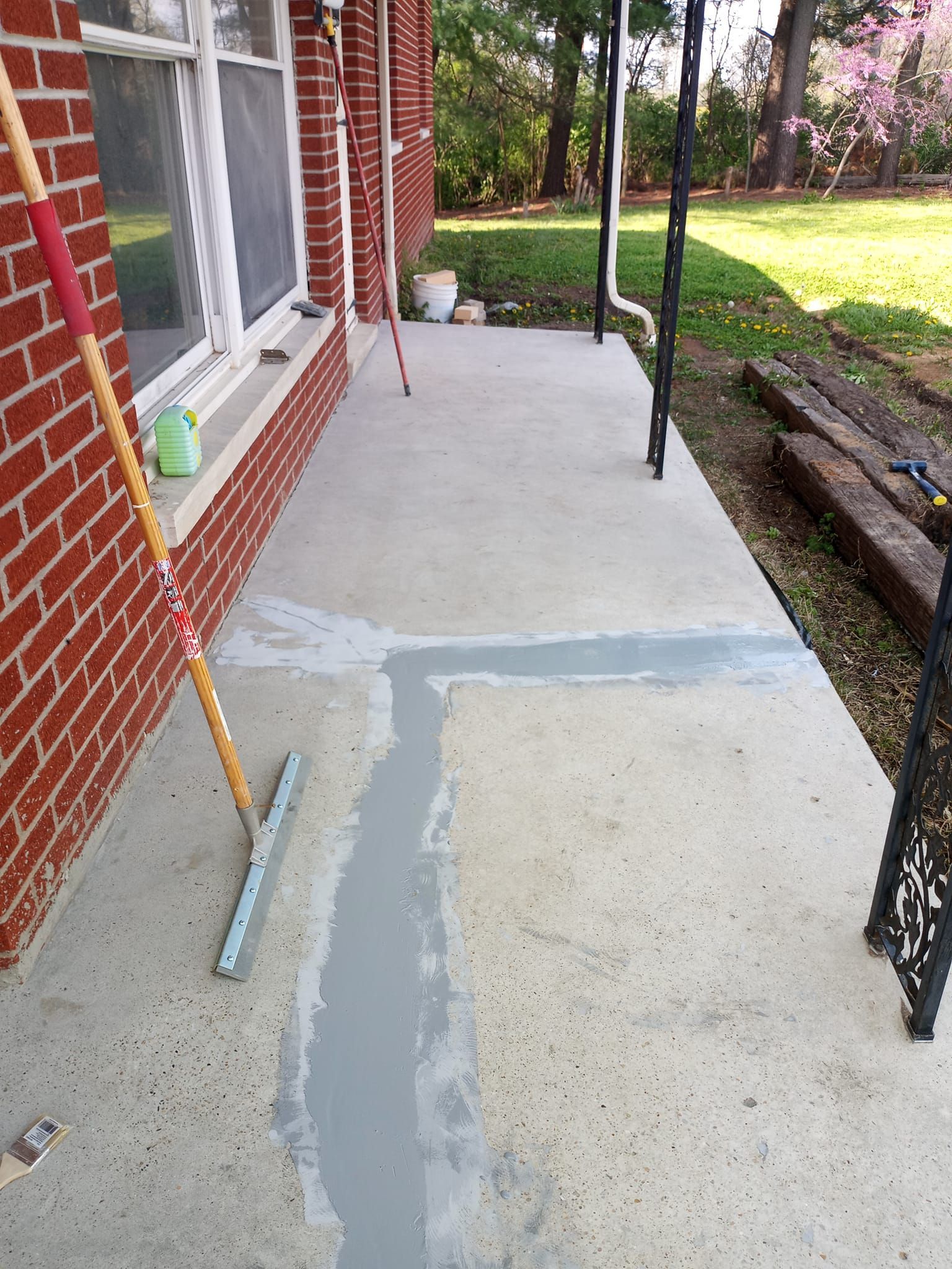 A brick-walled patio with light gray concrete, featuring fresh, wide sealant patches along a crack on the floor surface.