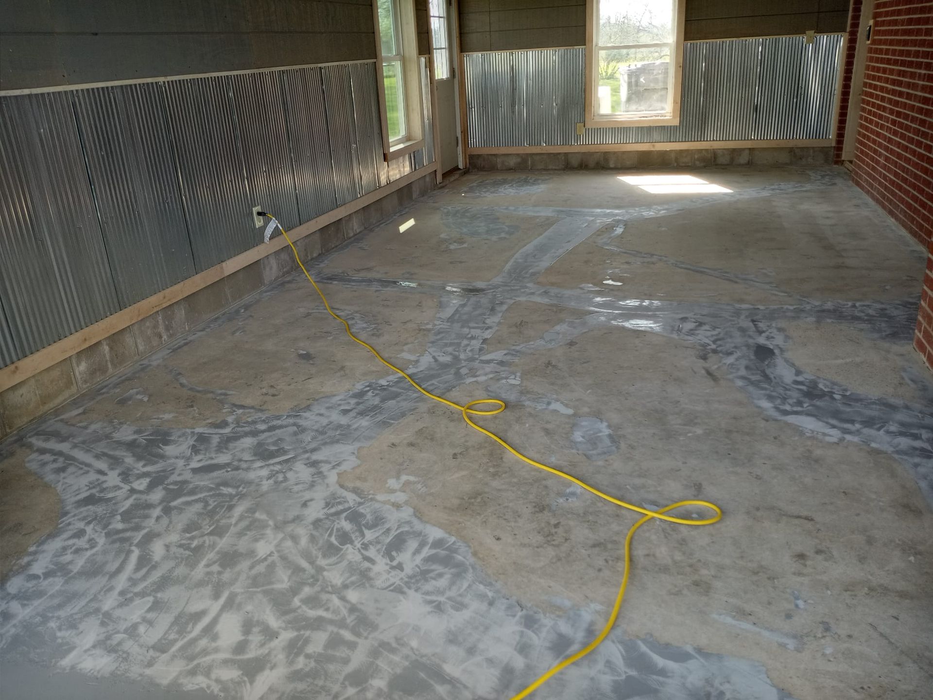 Concrete floor with patches of gray filler in a room featuring corrugated metal walls and a brick column.