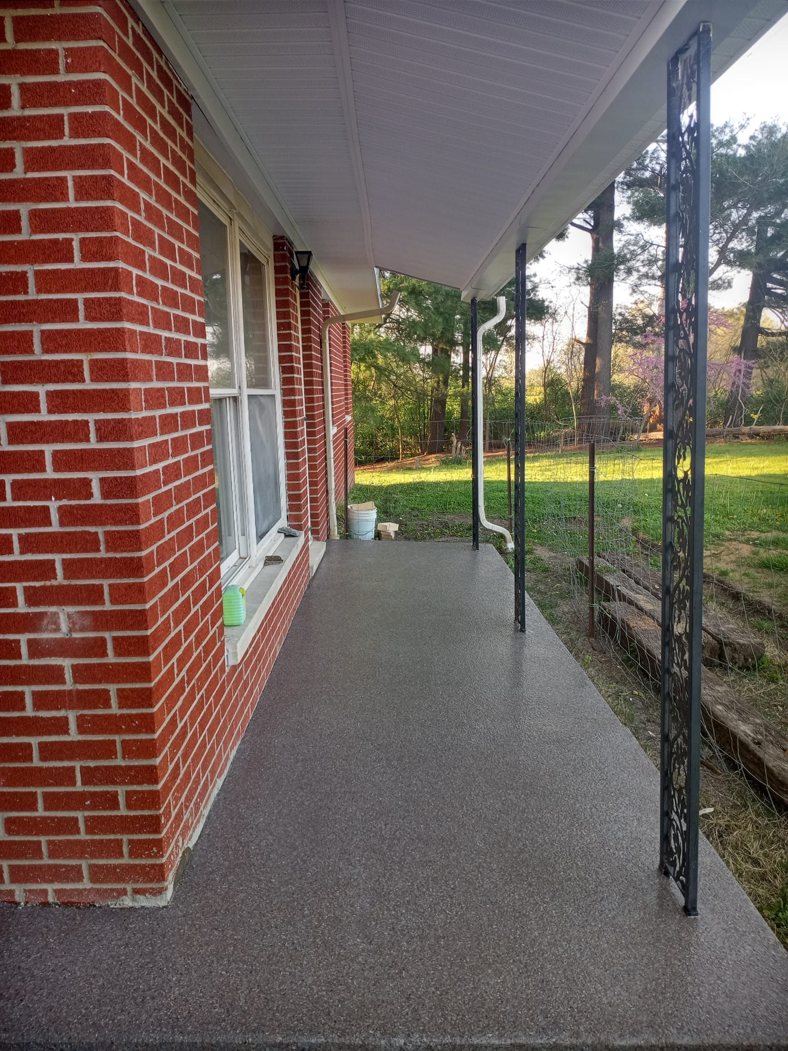 A brick-walled house with a clean, dark-speckled porch surface, white trim, and decorative metal support posts.