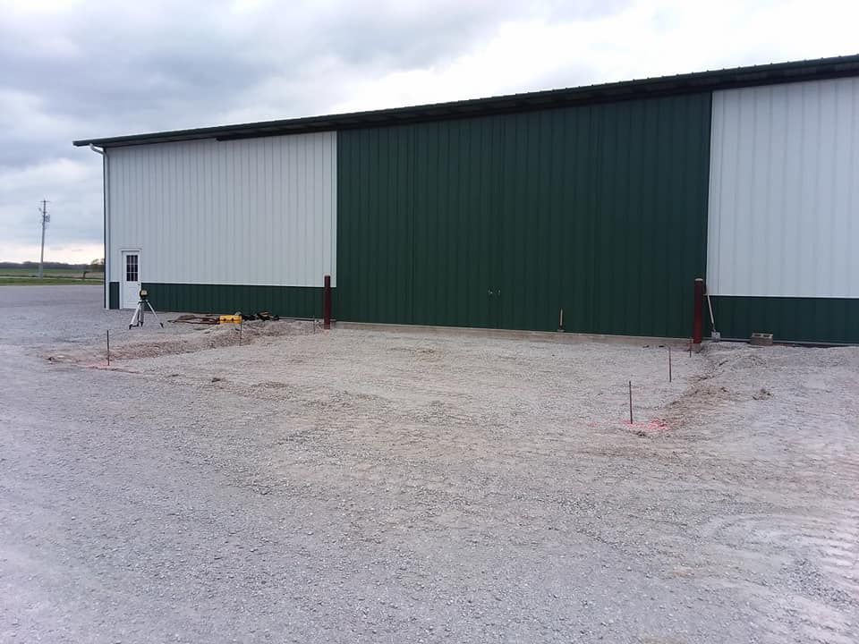 A large metal-sided building with white and green panels stands above a prepared gravel ground area.
