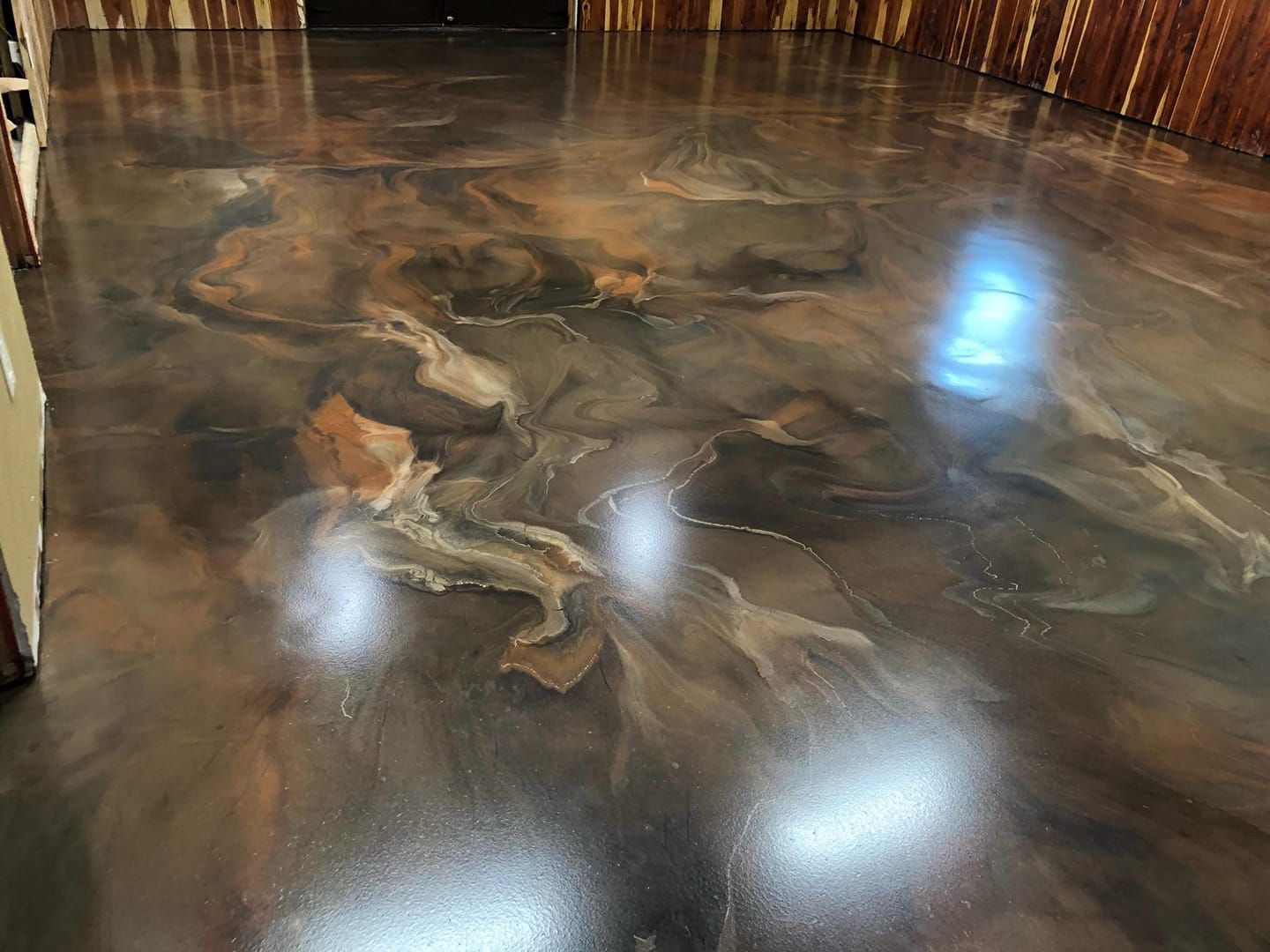 A glossy, brown and tan metallic epoxy floor with swirling patterns in a room with wood-paneled walls.