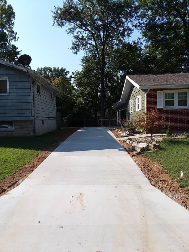 A newly poured concrete driveway runs between two single-story houses under a clear blue sky.