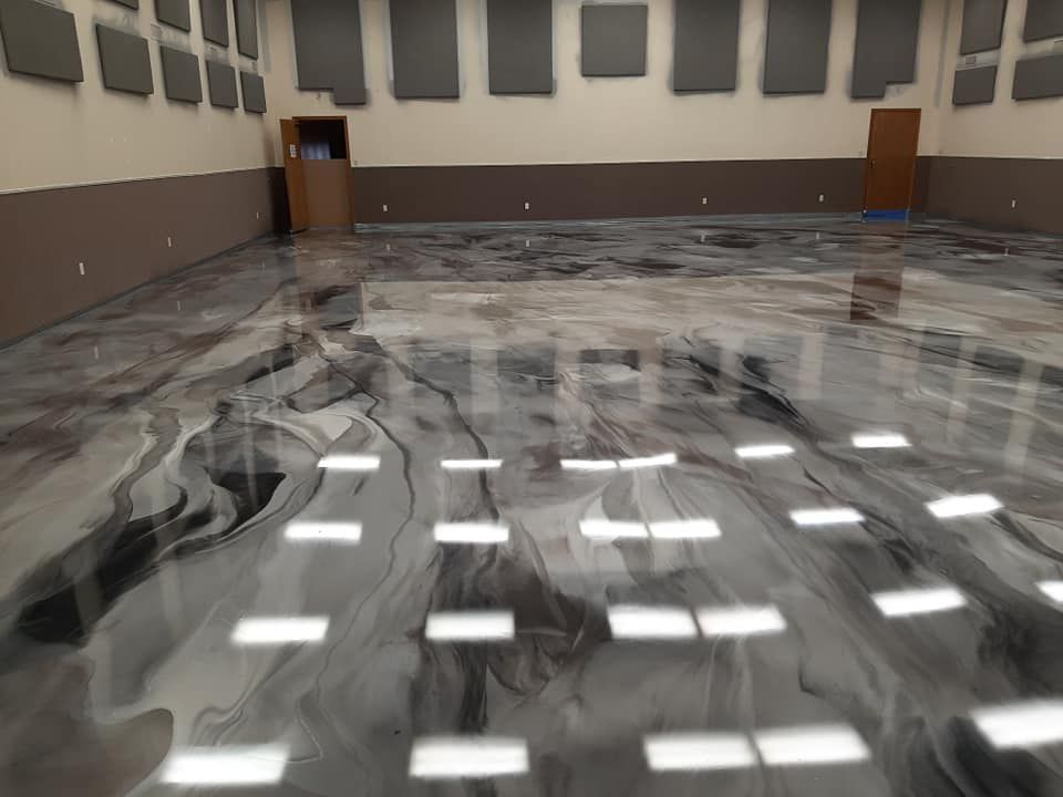 A spacious room features a glossy, marbled epoxy floor in shades of grey, black, and white with recessed ceiling lights.