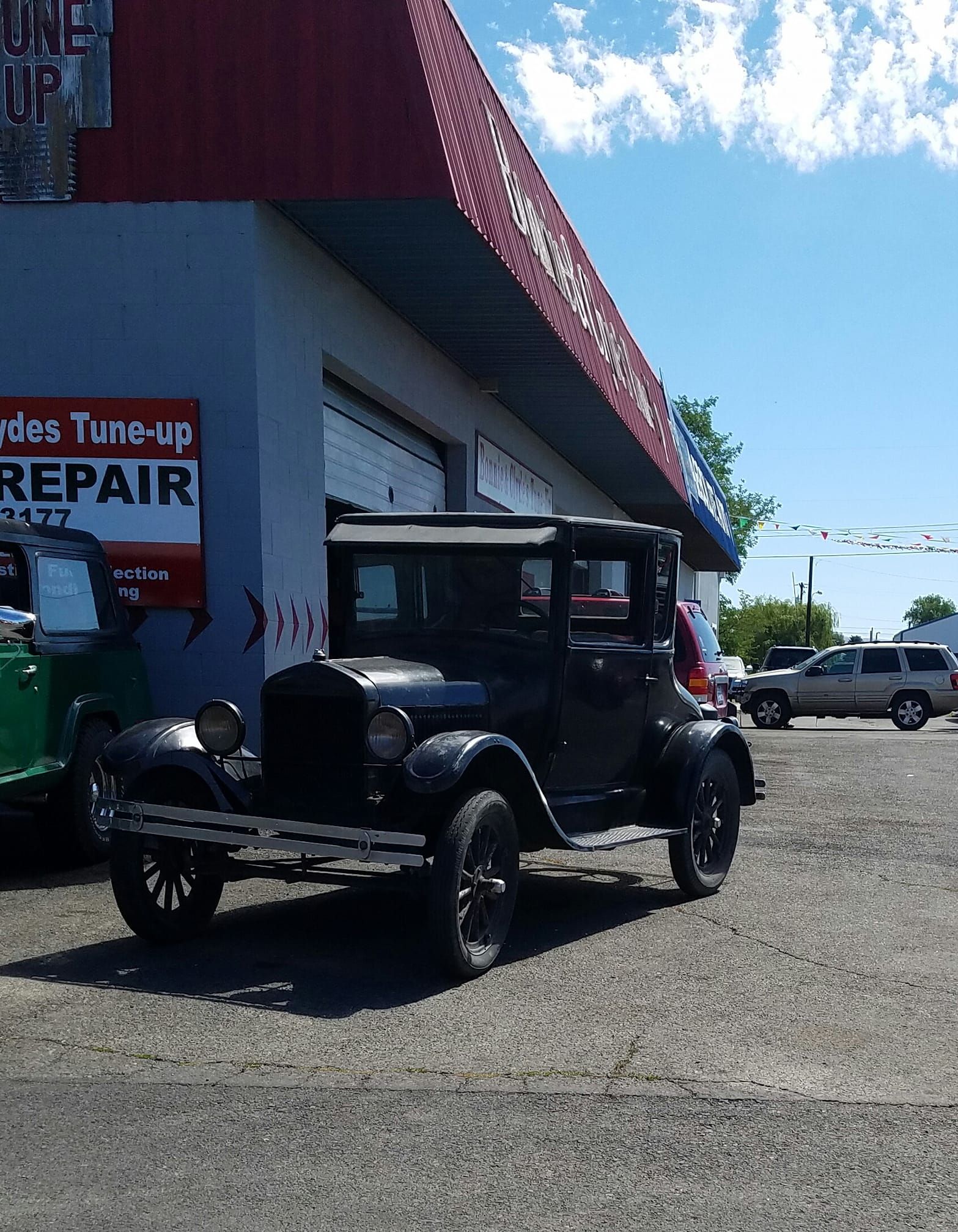 An old car is parked in front of a tune up repair shop