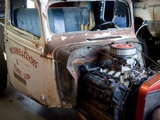 An old truck with a broken windshield is sitting in a garage.