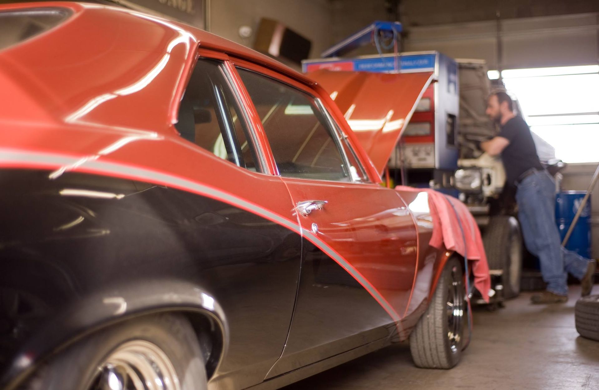 A man is working on a red and black car in a garage