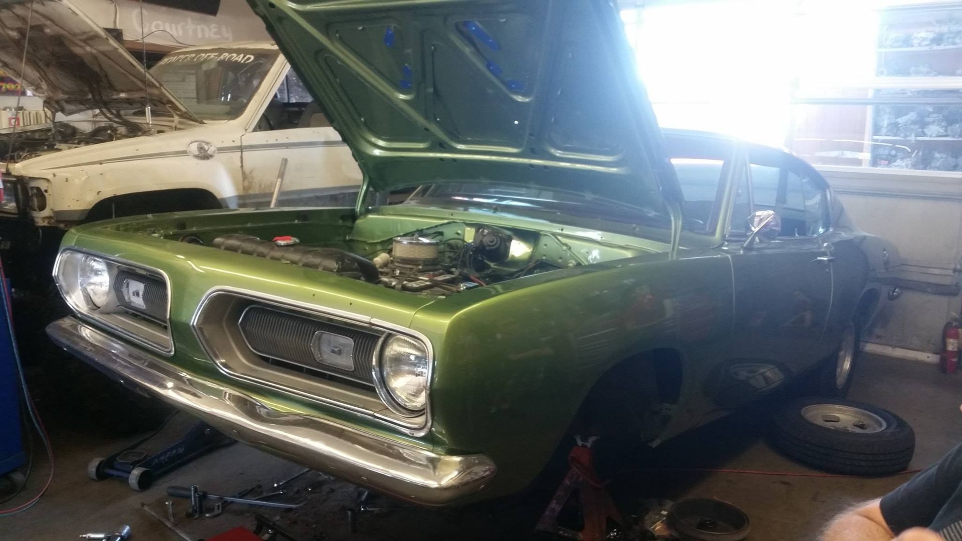 A green car with the hood up is sitting in a garage.