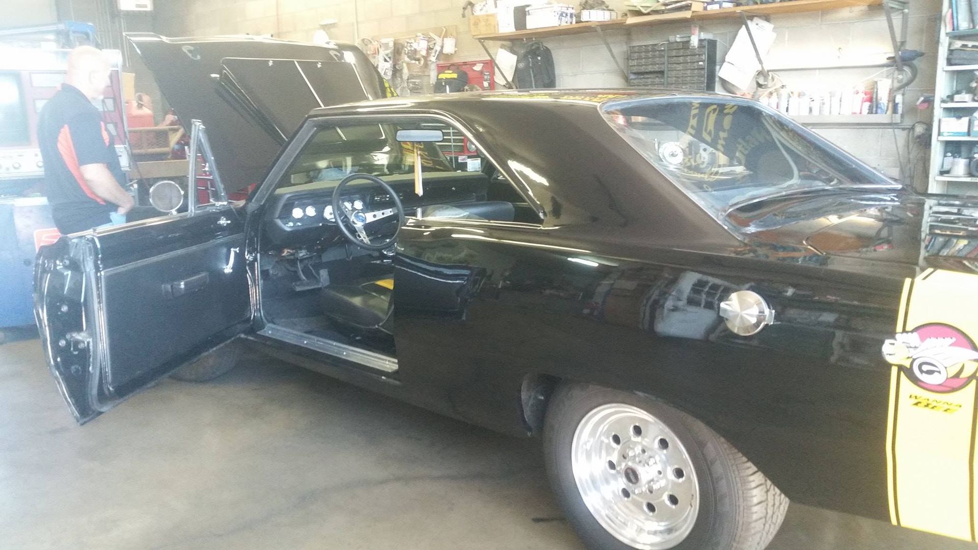 A black car with the hood open is parked in a garage.