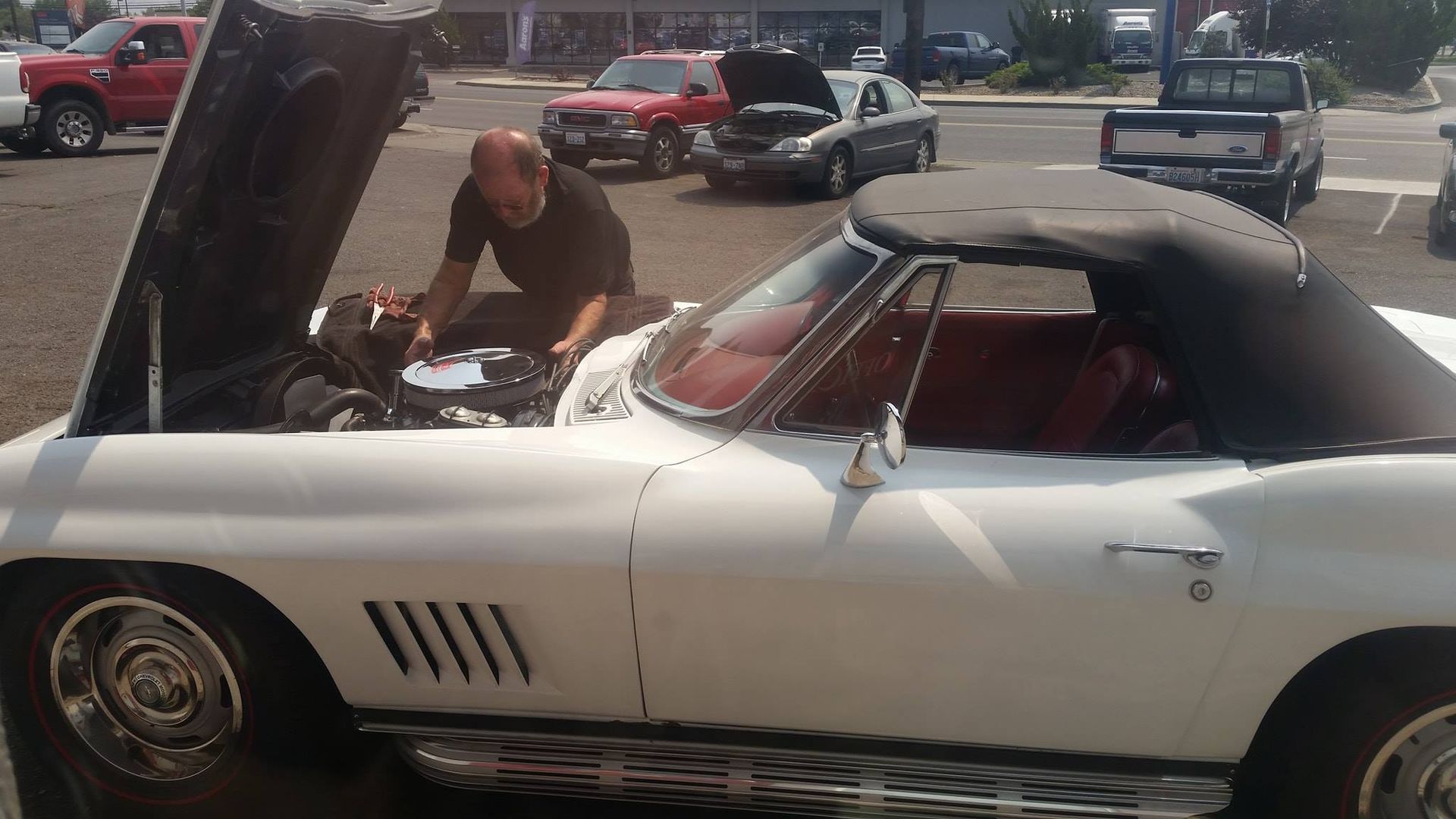 A man is working on a white car with the hood open