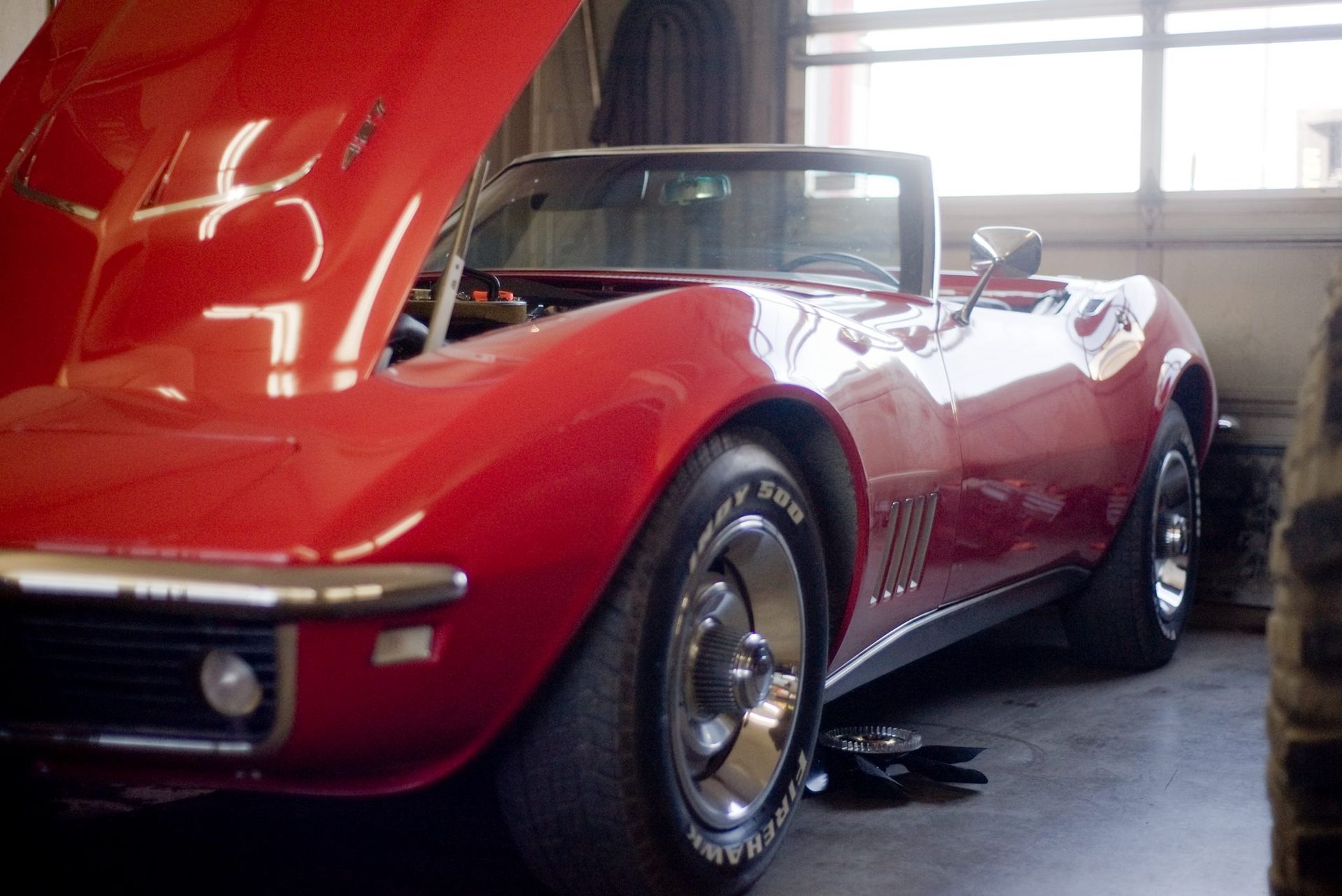 A red corvette with the hood up in a garage