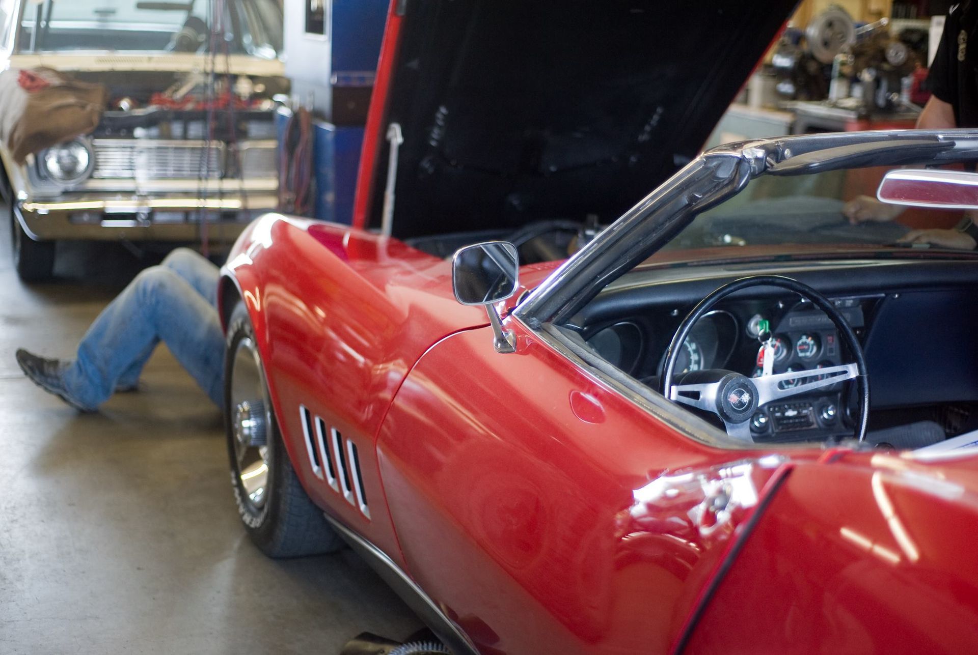 A man is working on a red corvette in a garage
