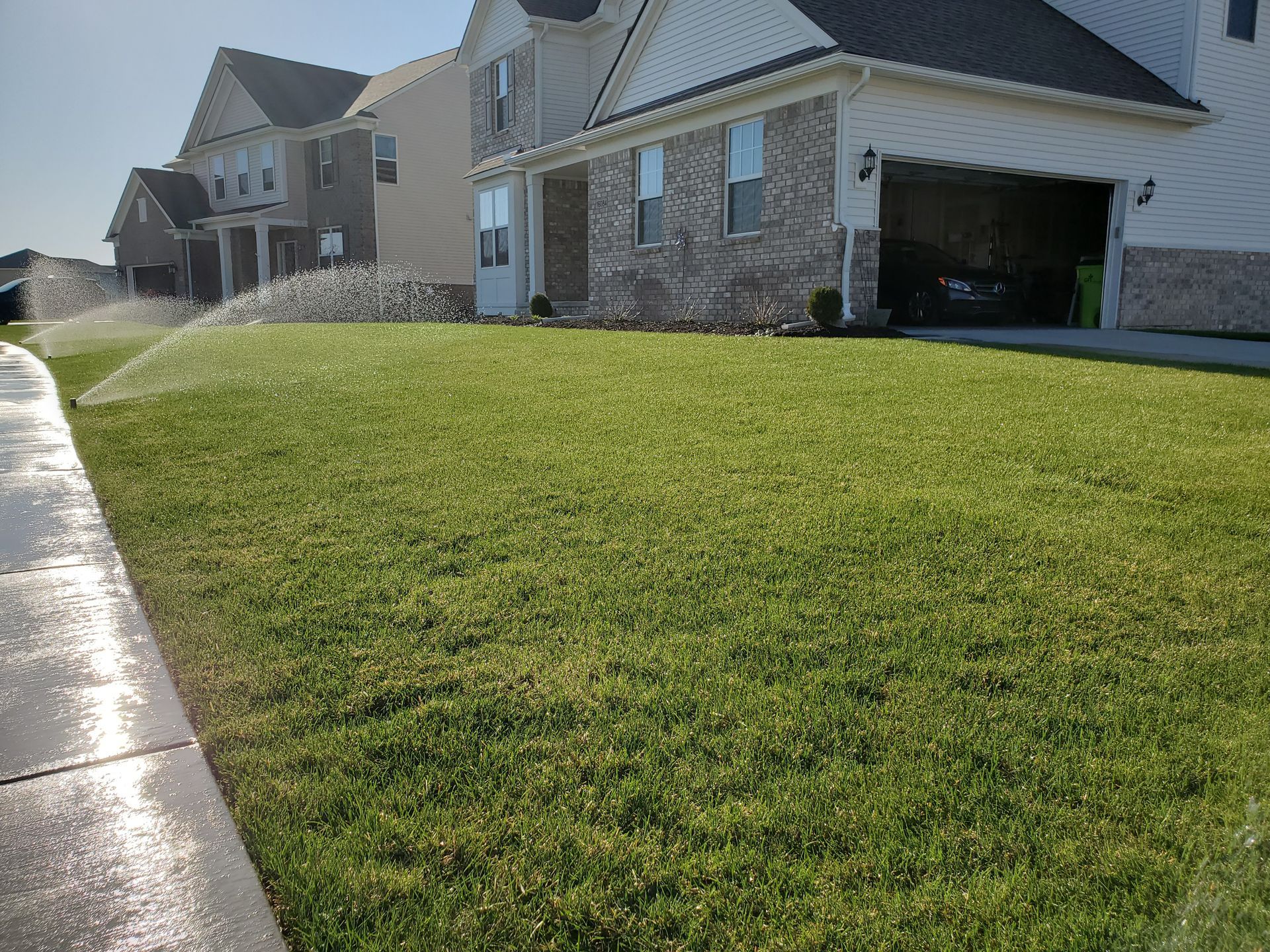 A sprinkler is spraying water on a lush green lawn in front of a house.
