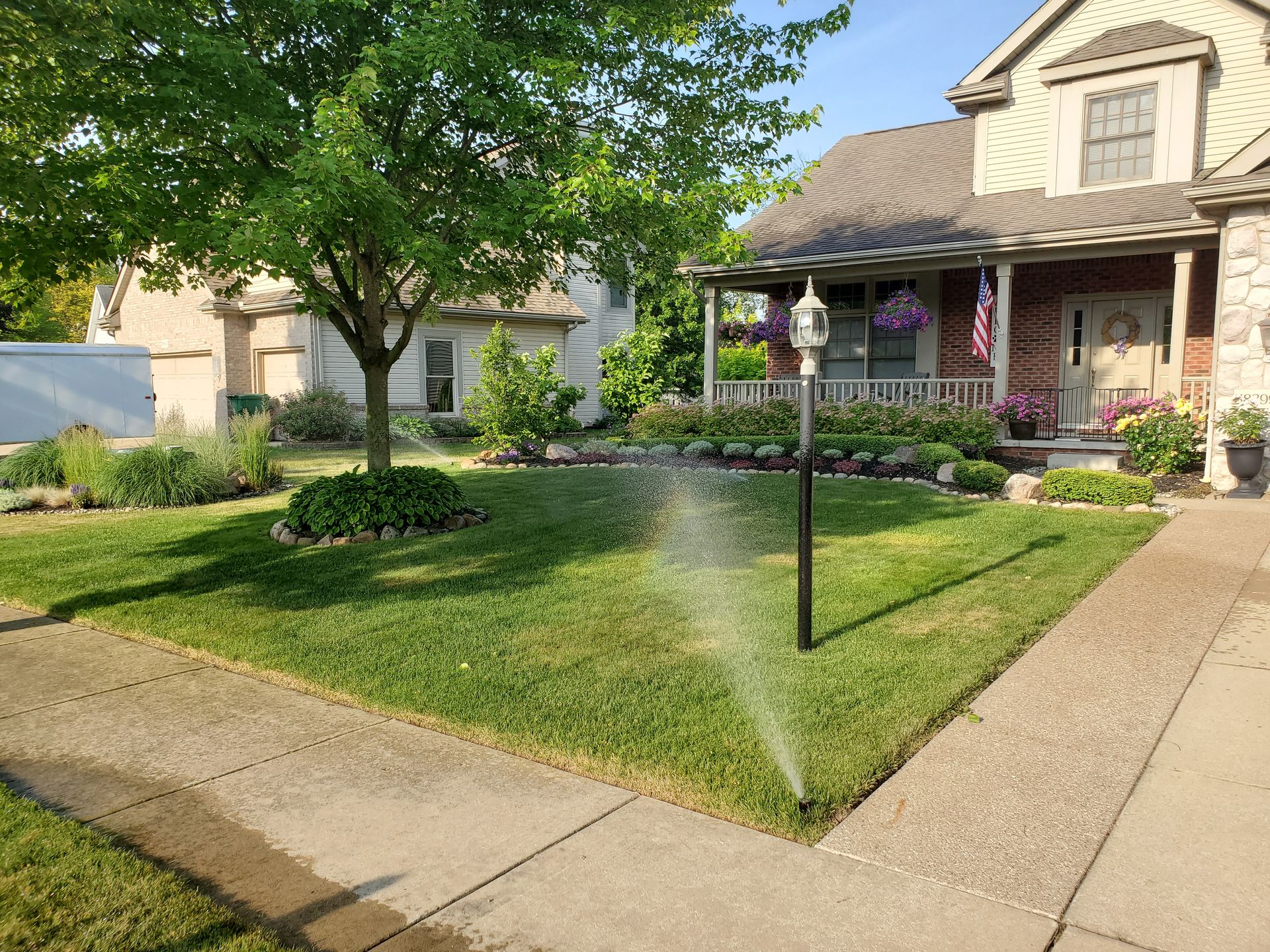 A lawn sprinkler is spraying water on a lush green lawn in front of a house.