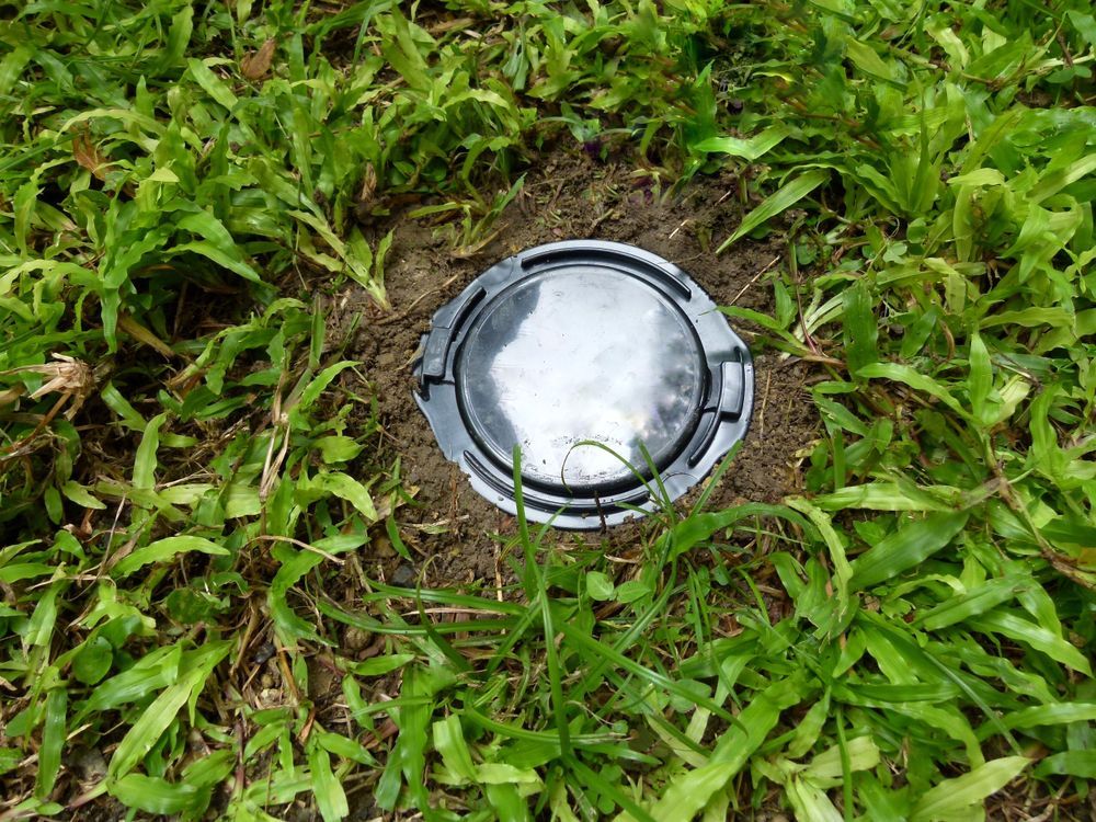 Black, circular utility cover set in grass and dirt — Bad Bugs Pest Control in Gracemere, QLD