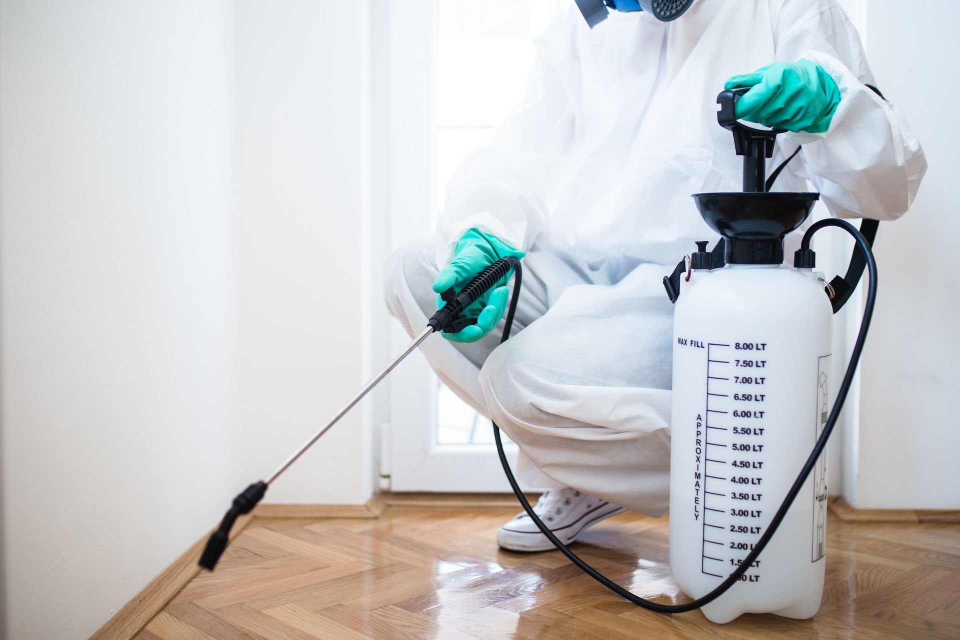 Person in protective suit spraying floor with a pesticide sprayer indoors — Bad Bugs Pest Control in Gracemere, QLD