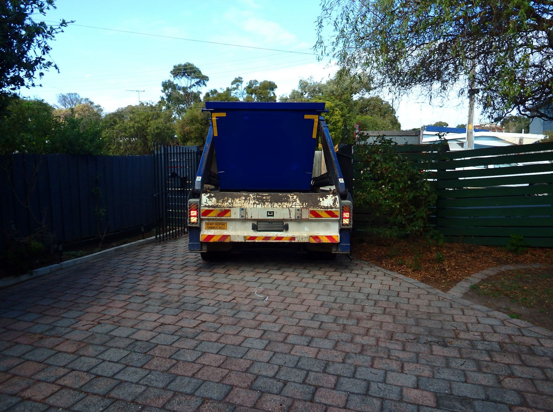 Blue Skip Bin on a Driveway, Surrounded by Fences and Foliage — Bad Bugs Pest Control in Rockhampton, QLD