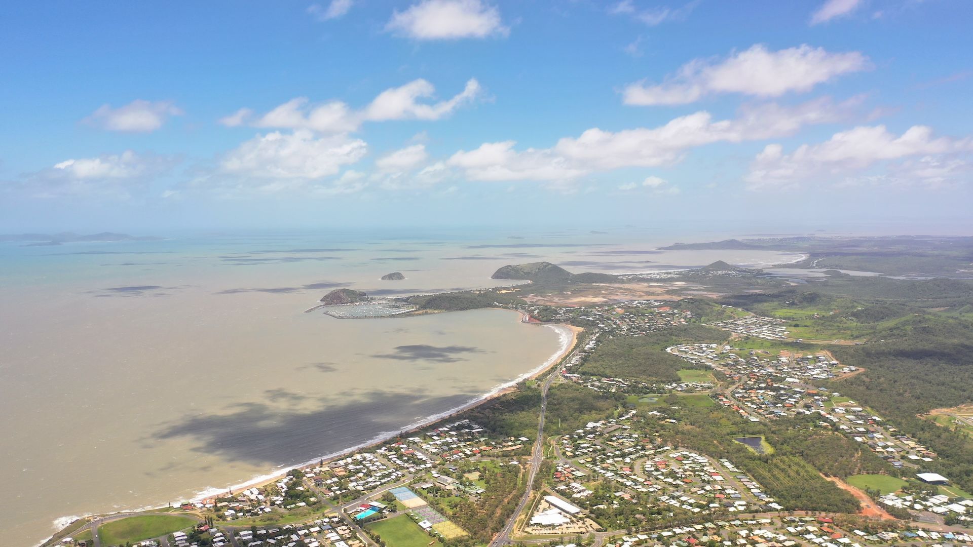 Aerial view of a coastal town with a beach, bay, and cloudy blue sky — Bad Bugs Pest Control in Gracemere, QLD
