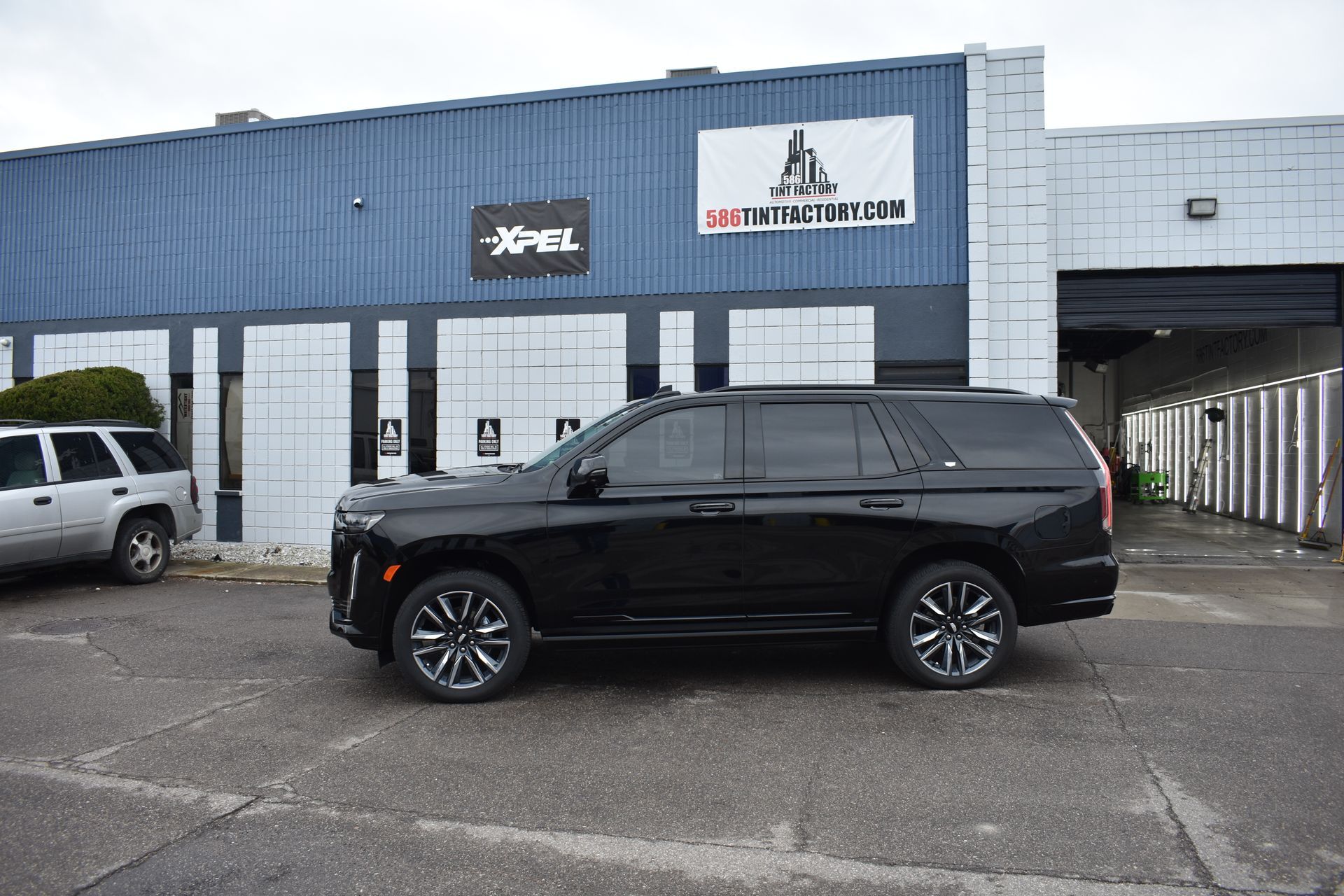 A black Cadillac Escalade parked in front of a blue building with an Xpel sign.