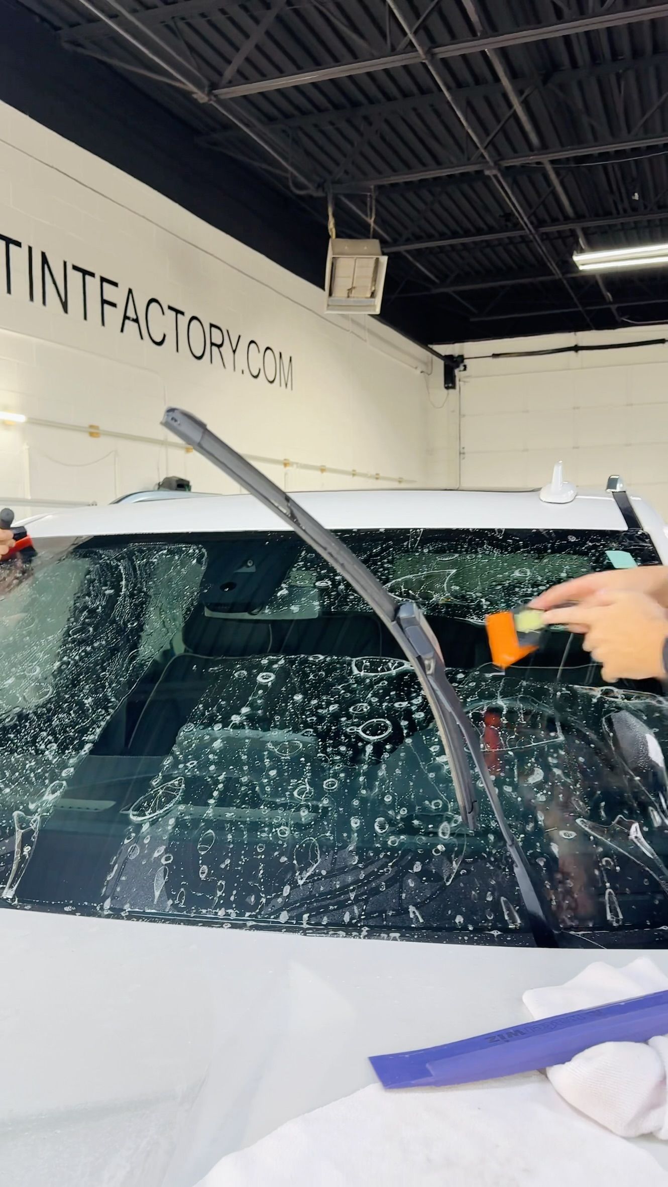 Person sprays orange tool onto shattered car windshield in workshop