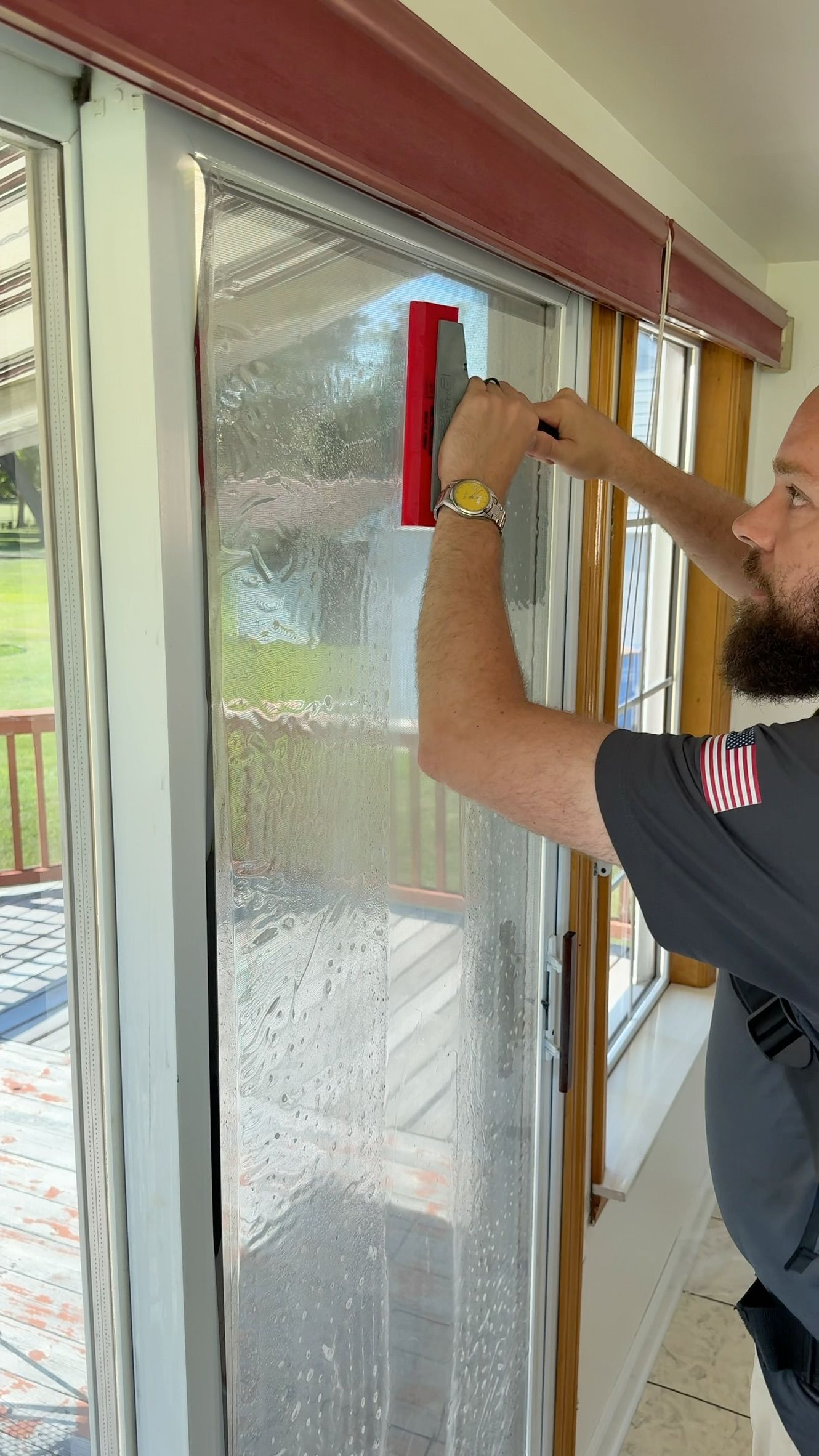 Person cleaning a glass door with a red squeegee in a hallway.