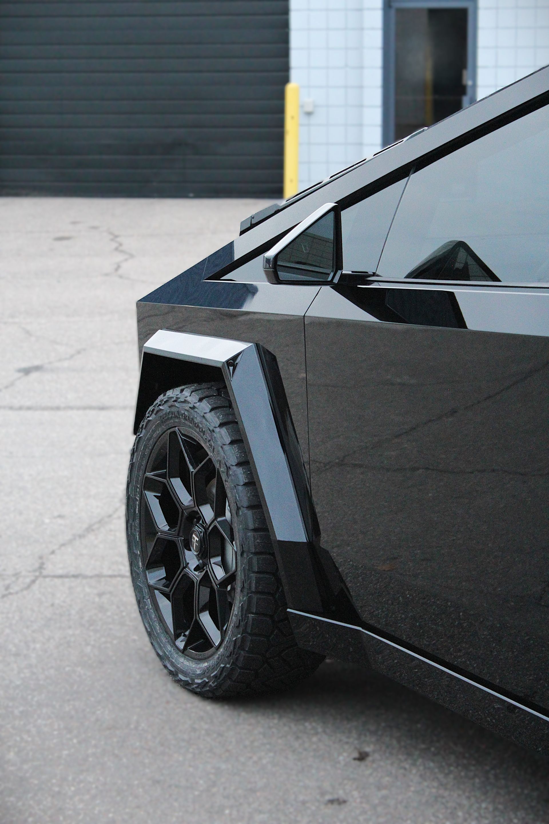 Black angular electric car close-up with black wheel parked beside a building.