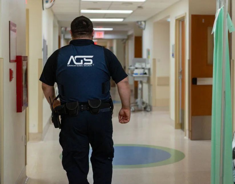 A security guard in a blue uniform walks down a brightly lit hospital corridor.