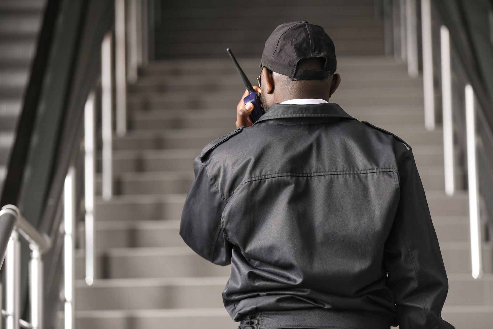 A man in a black jacket is talking on a walkie talkie while standing on a set of stairs.