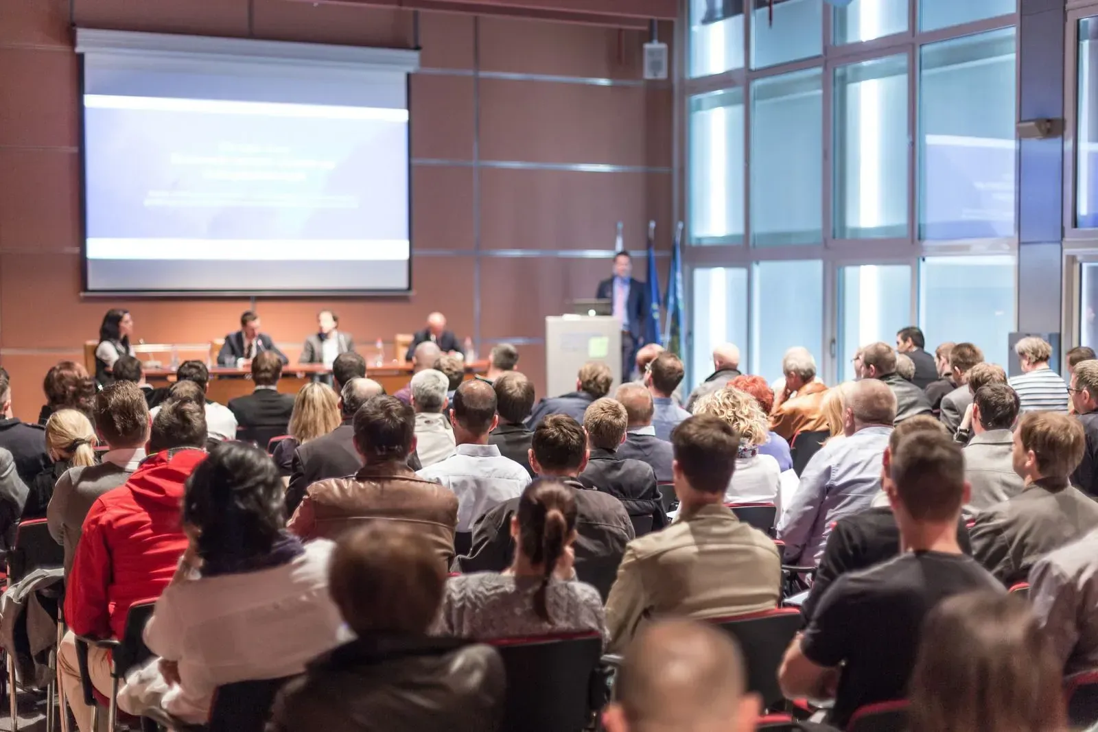 A large group of people are sitting in a conference room watching a presentation.