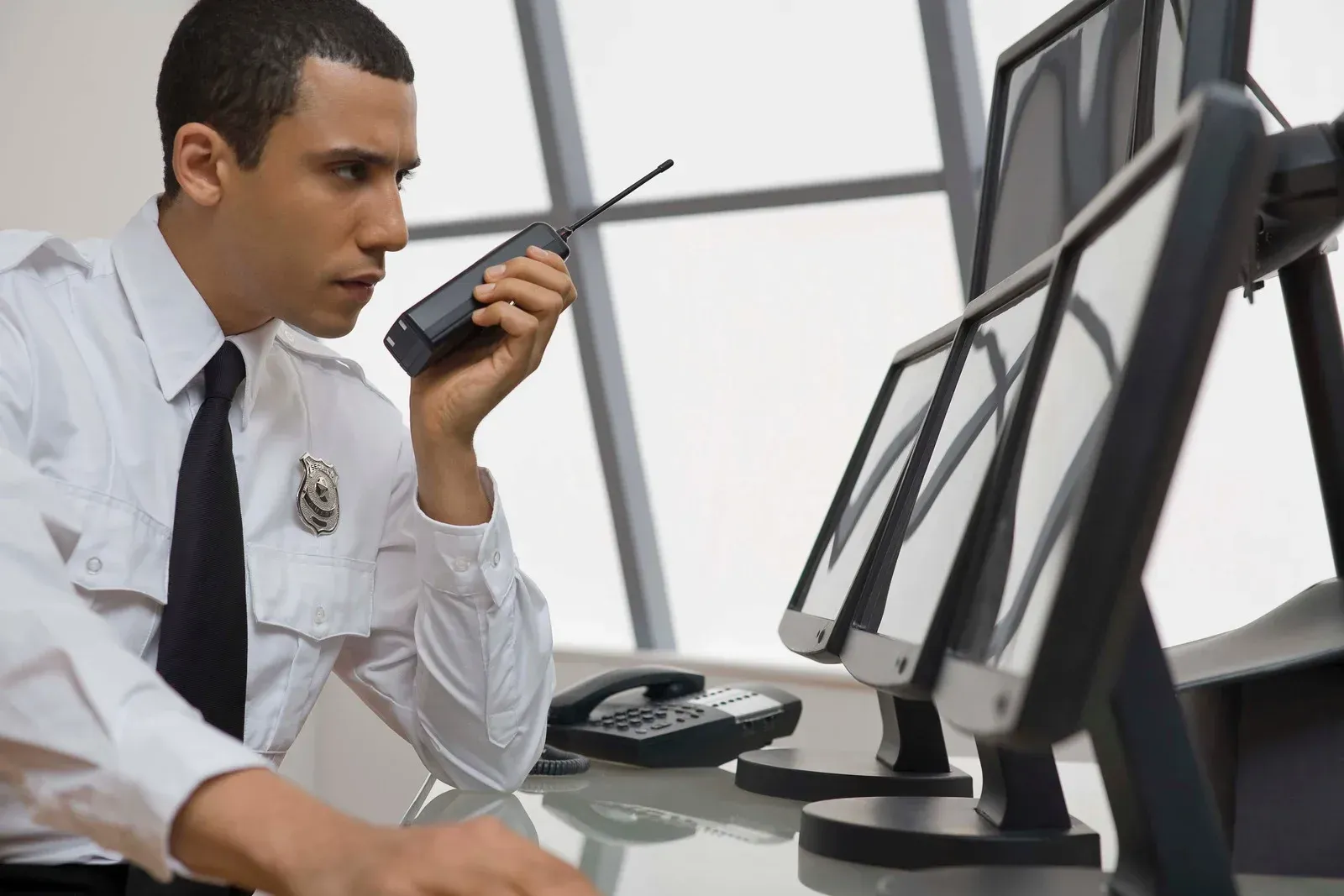 A man is sitting at a desk talking on a walkie talkie