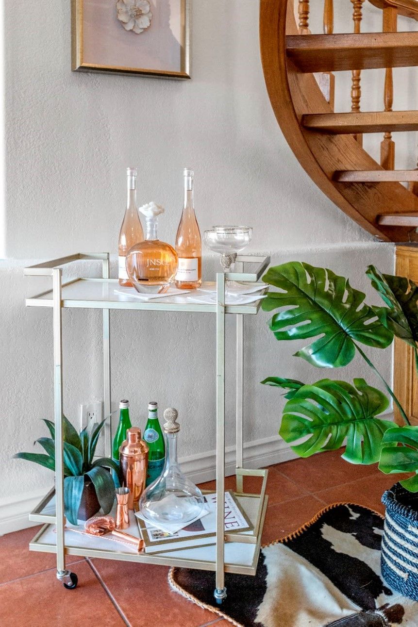 A bar cart with bottles of wine and glasses on it in a living room next to a spiral staircase