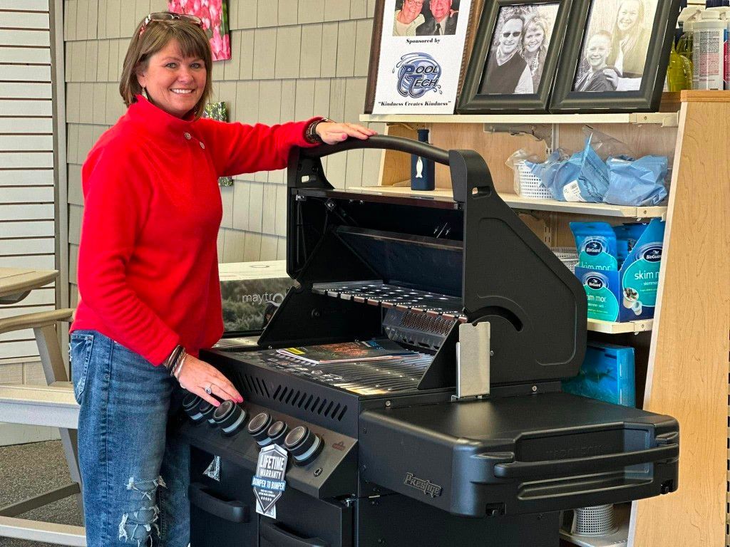 A woman in a red sweater is standing next to a grill.