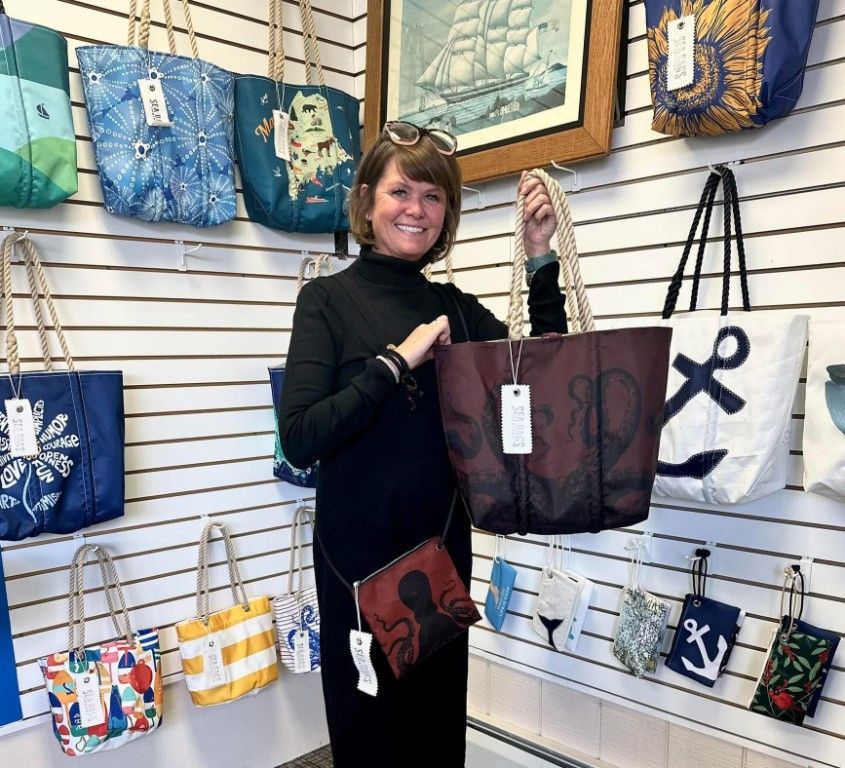 A woman is holding a tote bag in front of a wall of bags.