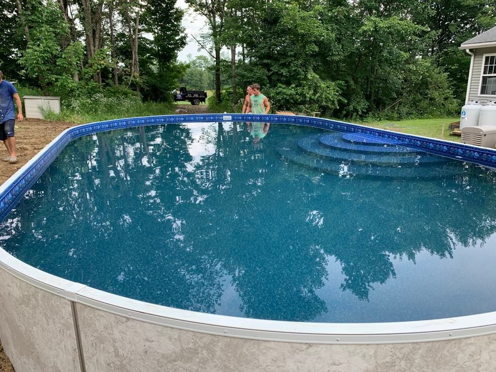 A man is standing next to a large swimming pool filled with blue water.