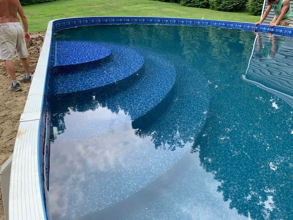 A man is standing next to a swimming pool with stairs.