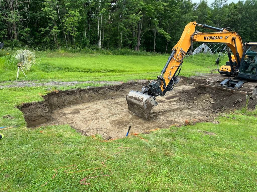 An excavator is digging a hole in the ground in a grassy field.