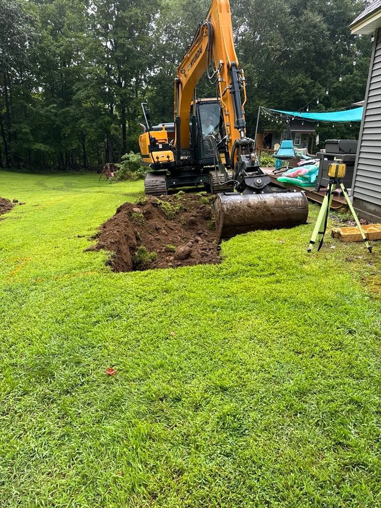 An excavator is digging a hole in the grass in a backyard.