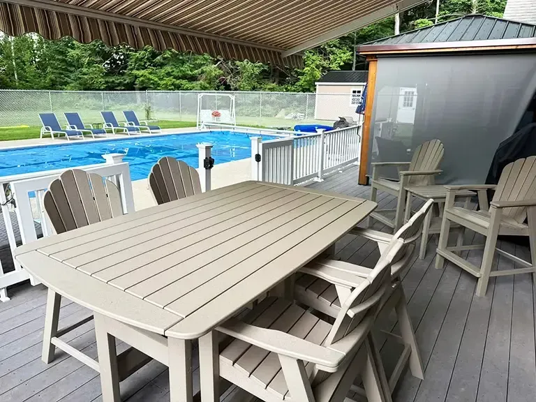 A table and chairs on a deck next to a swimming pool.