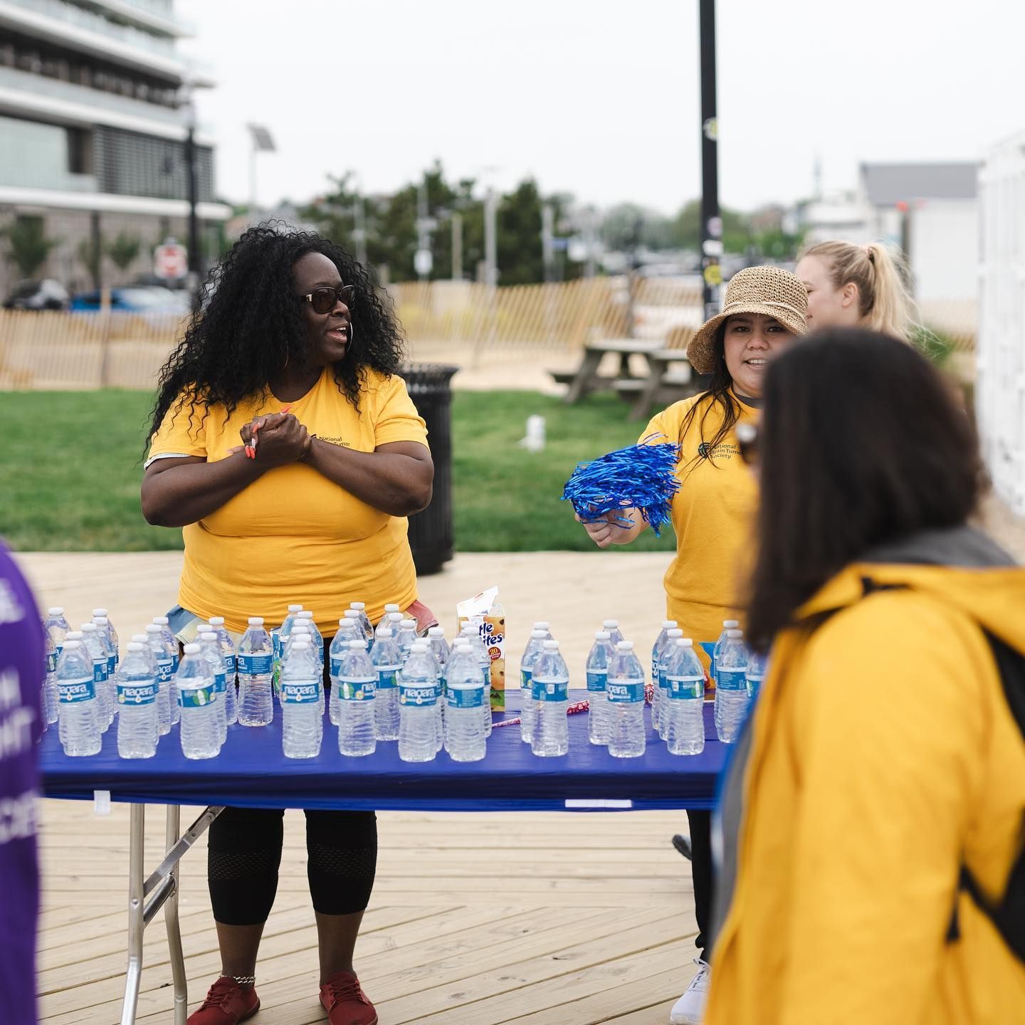 People at a water station, with water bottles on a blue table. One woman in yellow smiles.