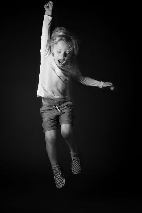 Child leaping joyfully, arm raised, mouth open, dark background.