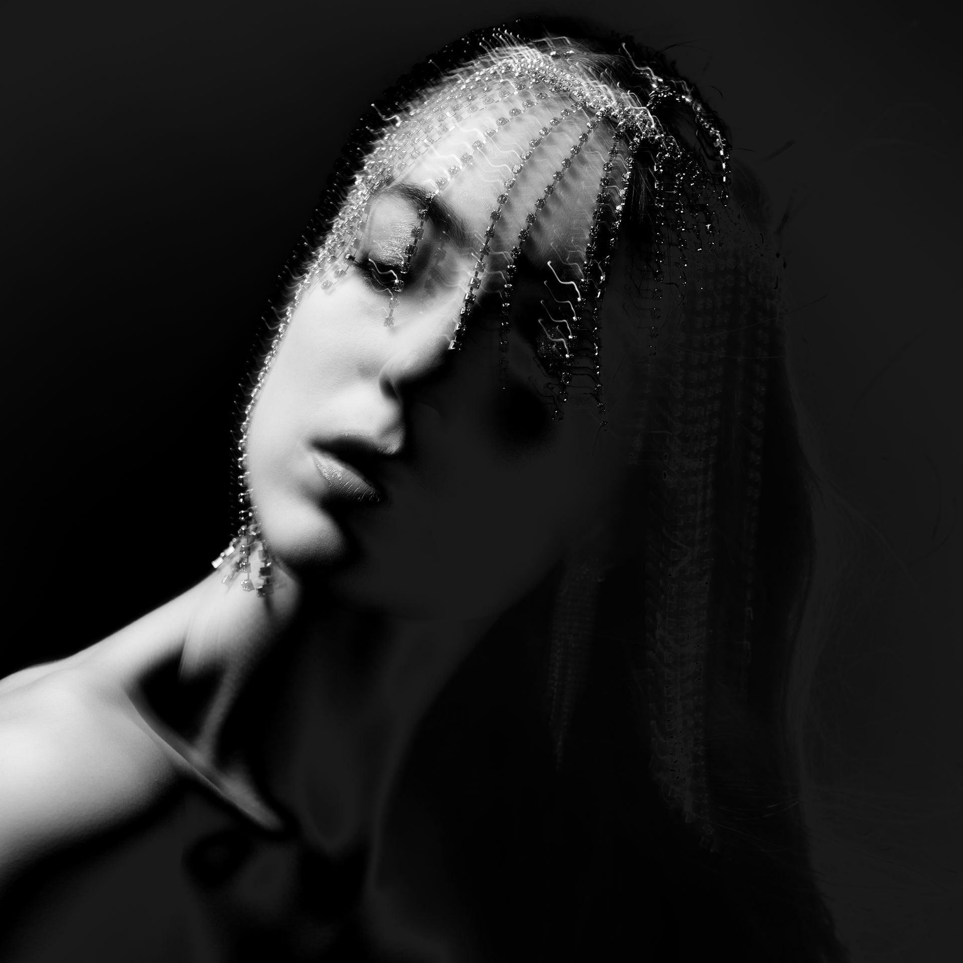 Woman with closed eyes, head tilted back, soft lighting. Headpiece detail, dark background.