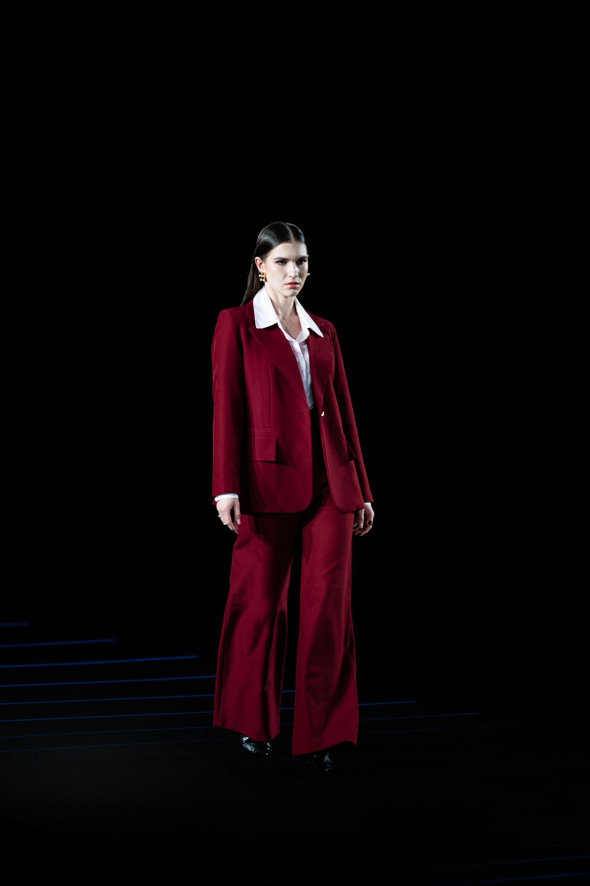 Woman in a red suit and white shirt, standing on a dark stage.