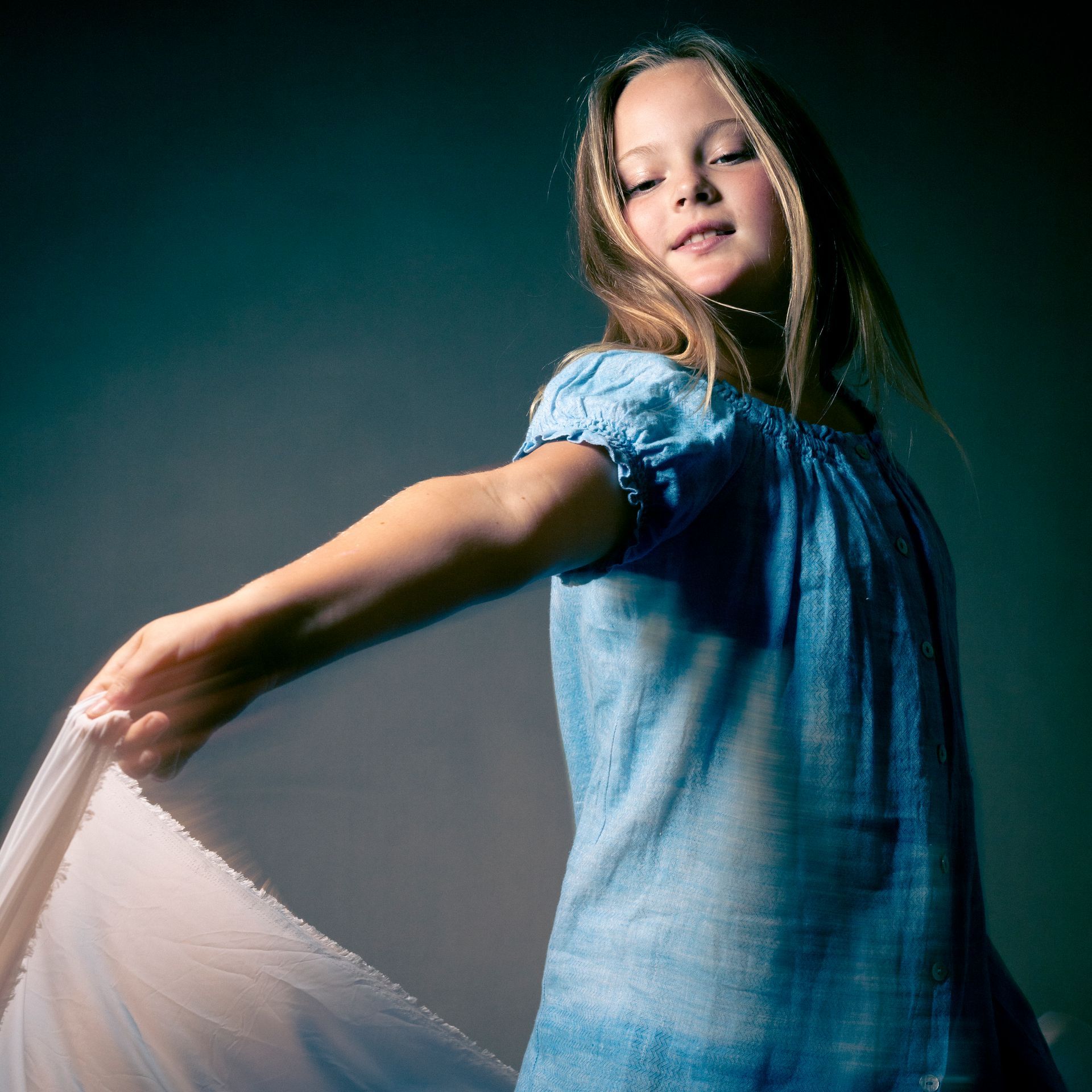 Young person in blue dress holding fabric, smiling, with an abstract background.