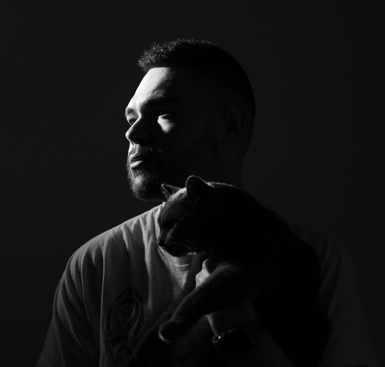 Man holding a cat, both silhouetted in dramatic lighting.