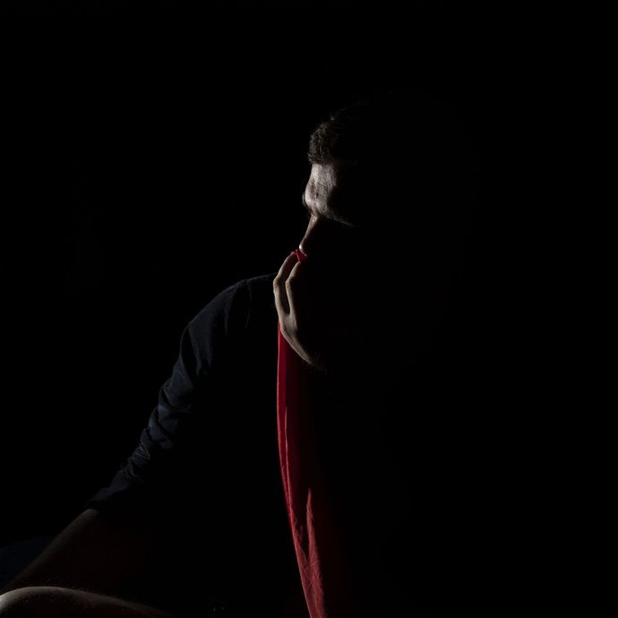 Silhouette of a person with the head and upper body visible, wearing a black shirt and red fabric.