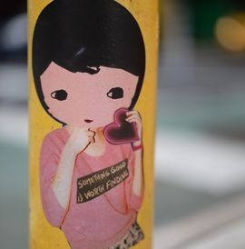 Cartoon girl holding a heart, wearing a pink shirt with text, on a yellow background.